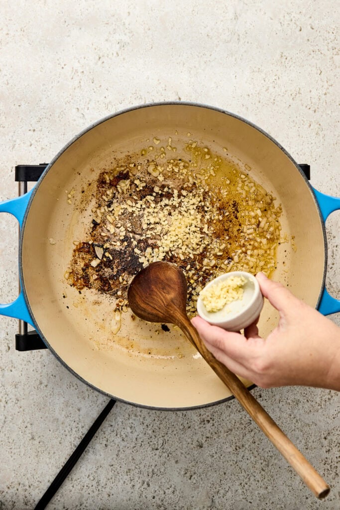 Cooking garlic and butter in a skillet for a creamy garlic butter sauce, with a hand adding minced garlic.