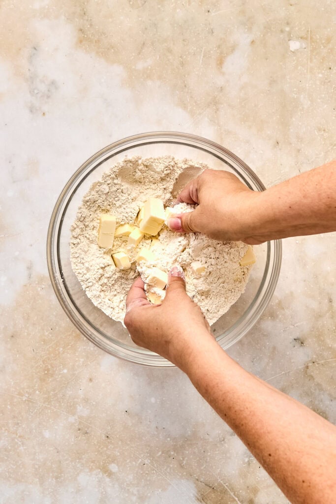 Hands mixing flour and butter in a glass bowl for baking, close-up of baking process at Stuck On Sweet.