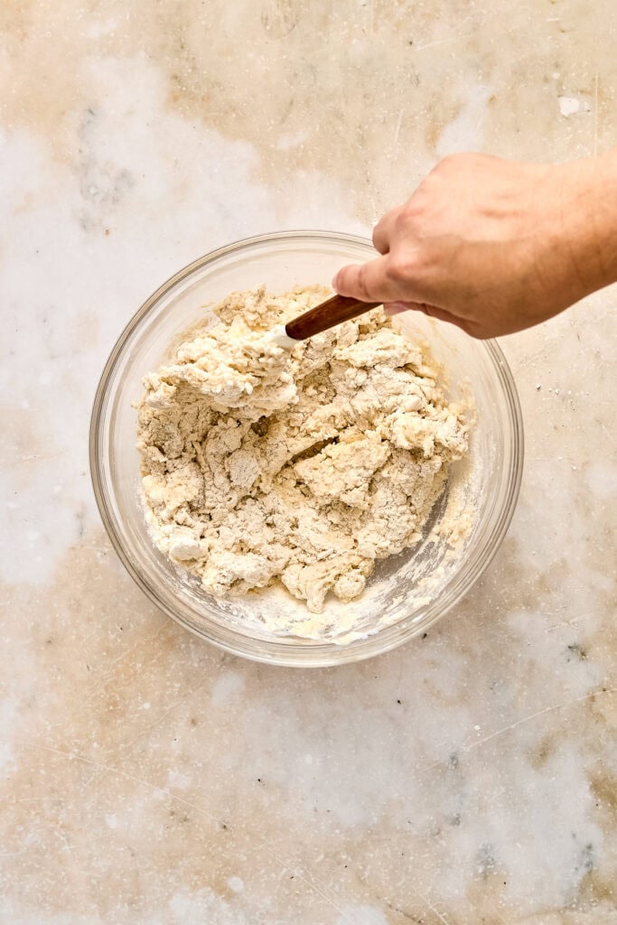 Hand stirring dough in a glass bowl with a wooden spoon, ready for baking sweet desserts.