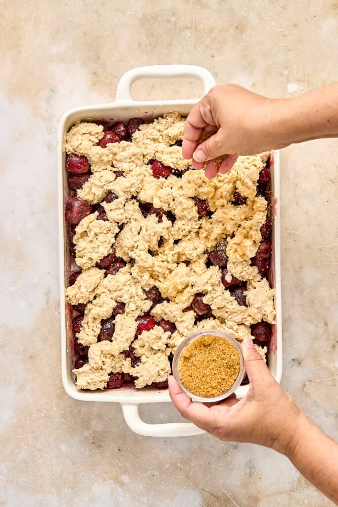 Preparing cherry cobbler with a crumbly streusel topping in a baking dish, ready for baking or serving.