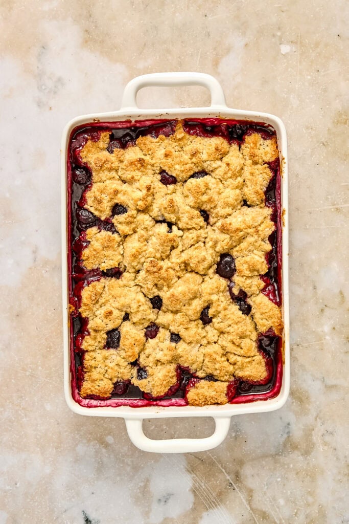 Delicious homemade cherry cobbler with a golden crumb topping in a white baking dish, ready to serve.