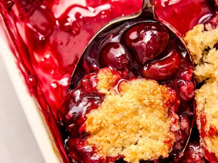 Close-up of a cherry cobbler dessert with a spoonful showing cherries, berries, and a crumbly topping, perfect for sweet cravings.