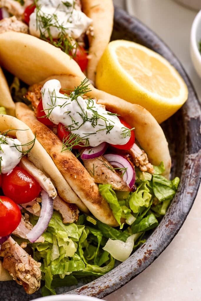 Geek yogurt marinated chicken pitas on a dark plate with greens, tomatoes and tzatziki sauce.