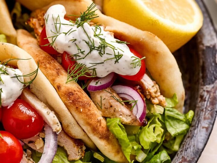 Geek yogurt marinated chicken pitas on a dark plate with greens, tomatoes and tzatziki sauce.