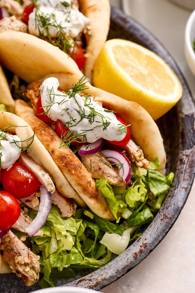 Geek yogurt marinated chicken pitas on a dark plate with greens, tomatoes and tzatziki sauce.