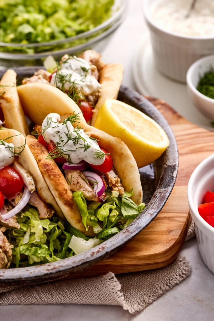 Delicious chicken pita sandwich filled with seasoned meat, fresh vegetables, and creamy sauce, served with lemon wedge on a rustic plate. Perfect for a flavorful Mediterranean meal.