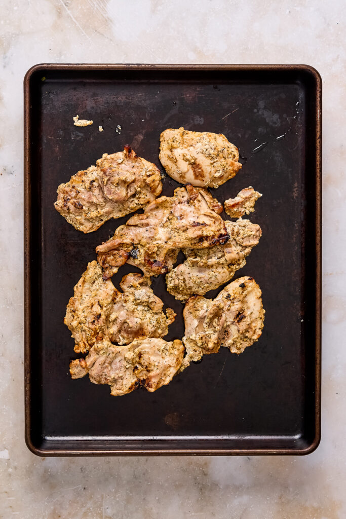 cooked yogurt marinated greek chicken thighs on a black sheet pan.