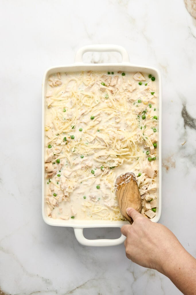 Baked creamy chicken and orzo casserole topped with shredded cheese and green peas in a white baking dish, ready to serve.