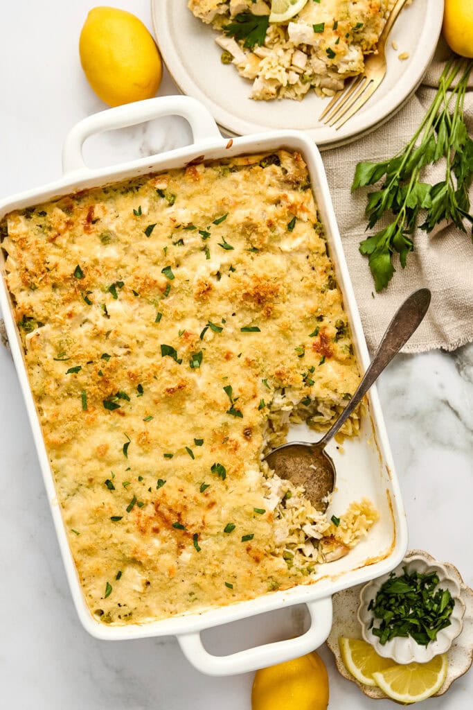 Delicious cream lemon chicken orzo casserole with a golden, crispy topping, served in a white baking dish, garnished with fresh herbs and lemon slices.