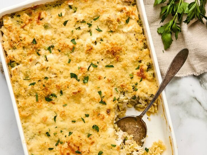 Delicious cream lemon chicken orzo casserole with a golden, crispy topping, served in a white baking dish, garnished with fresh herbs and lemon slices.