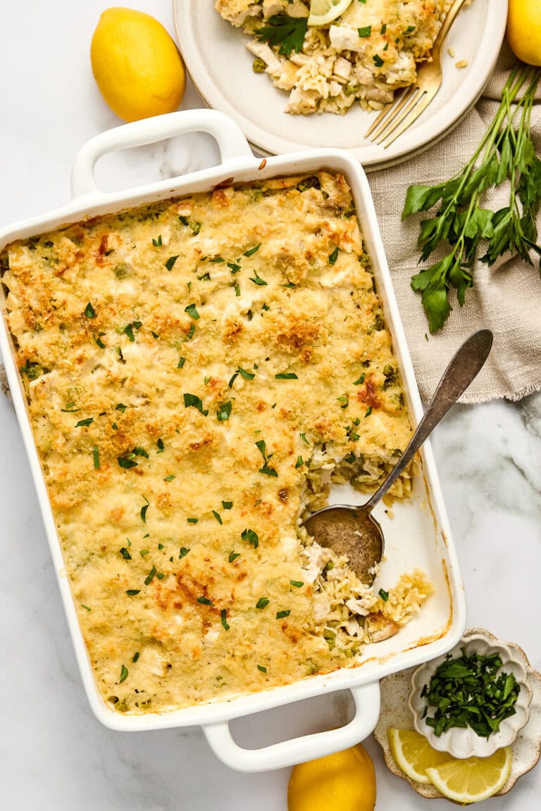 Delicious cream lemon chicken orzo casserole with a golden, crispy topping, served in a white baking dish, garnished with fresh herbs and lemon slices.