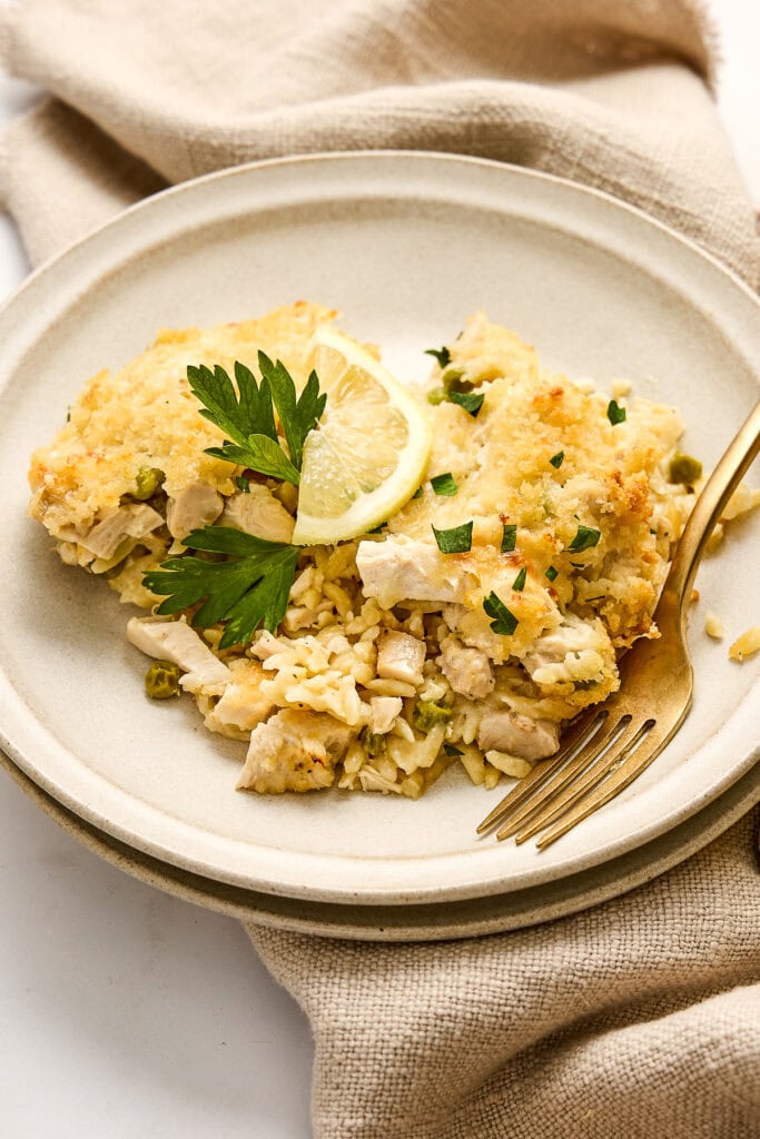 Delicious creamy lemon baked chicken and orzo with peas with golden breadcrumbs, garnished with lemon slices and fresh parsley, served on a neutral ceramic plate.