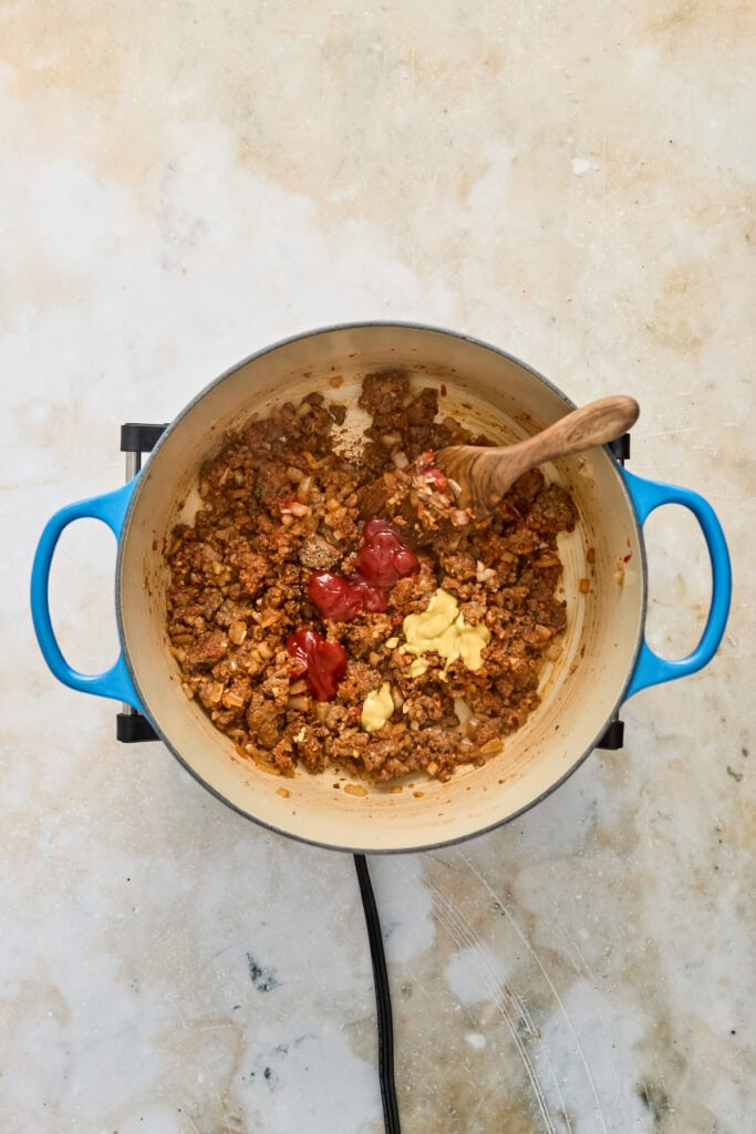 A pot of cooked ground beef with tomatoes and butter, ready for serving, on a light-colored surface.