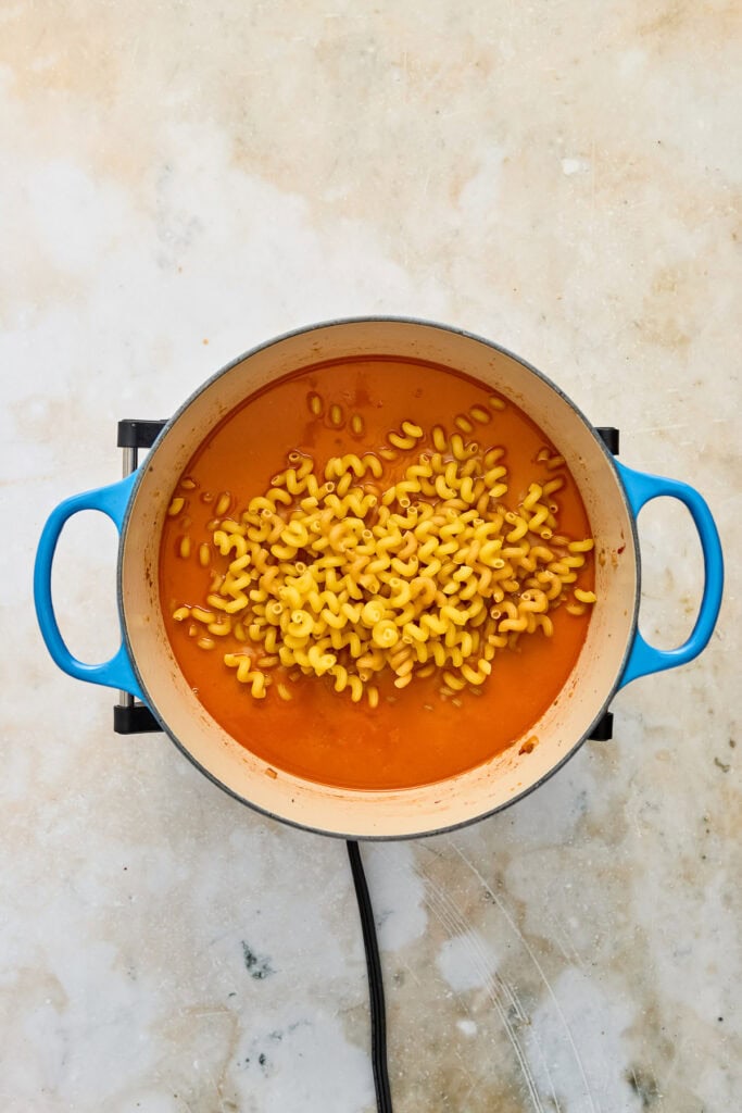 Boiling pasta in a blue pot with orange sauce, viewed from above, on a light-colored surface.