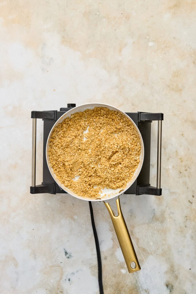 Close-up of toasted breadcrumbs in a frying pan on a stovetop, ready for cooking or garnishing.