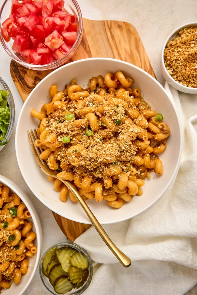 Delicious creamy cheeseburger pasta topped with golden breadcrumbs, served in a white bowl with fresh tomato and pickle sides, perfect comfort food.