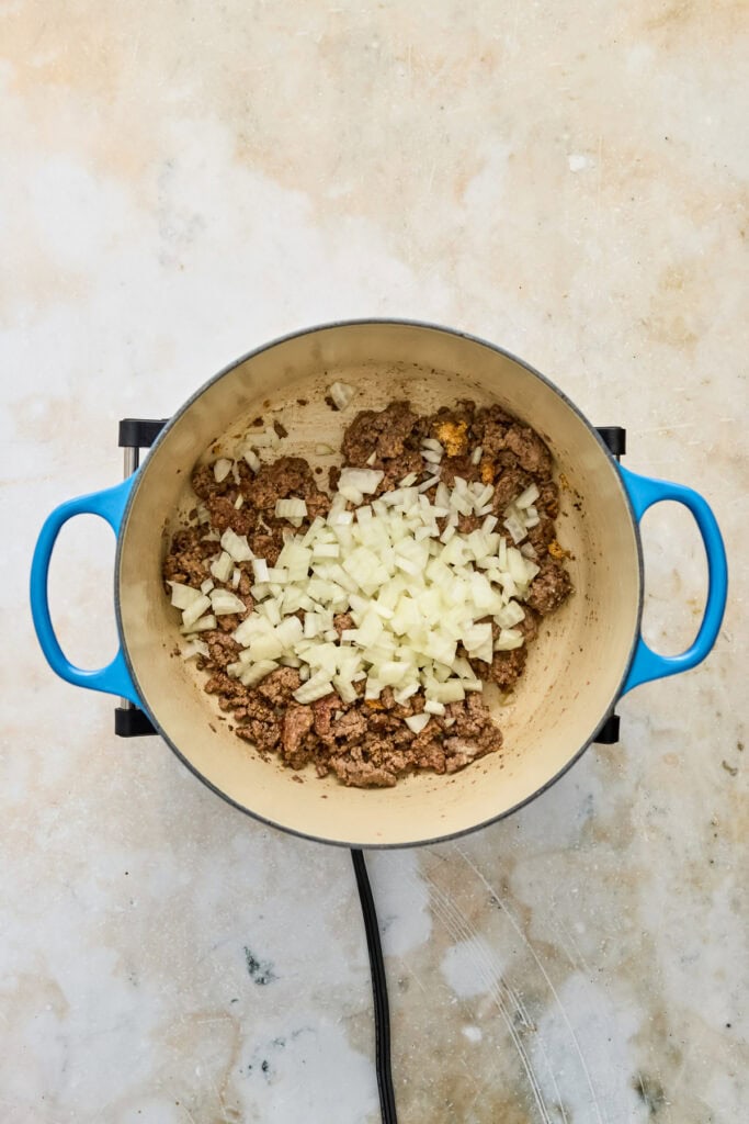 Ground beef and chopped onions cooking in a blue pot on a stovetop, ready for a delicious meal.