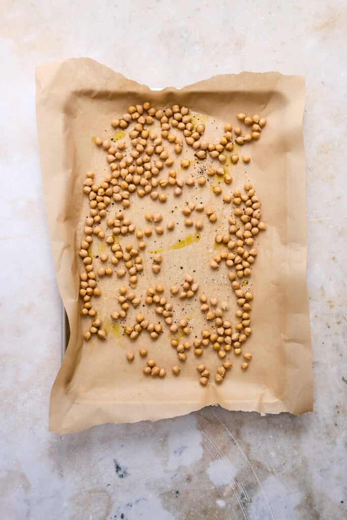 Uncooked roasted chickpeas spread on parchment paper, ready for baking, with a light background.