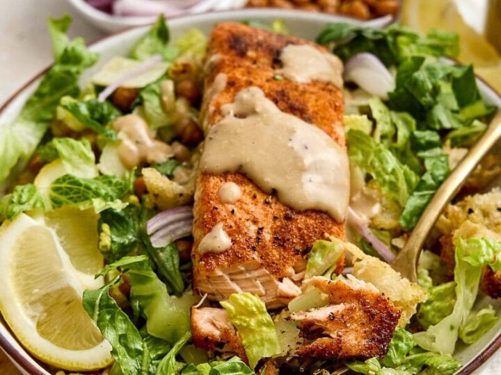 Delicious crispy salmon Caesar salad with roasted chickpeas, garlic Parmesan croutons, fresh greens, lemon wedges, and creamy dressing, perfect for a healthy meal.