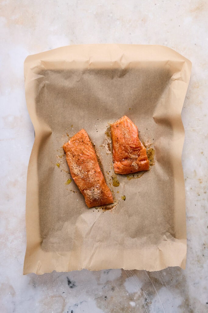 Two baked salmon fillets on parchment paper, seasoned and cooked to perfection, ready for serving.