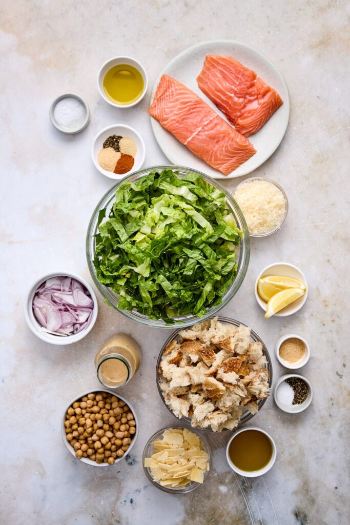 Fresh salmon fillets, romaine lettuce, roasted chickpeas, garlic Parmesan croutons, and salad dressing ingredients for a delicious Caesar salad.