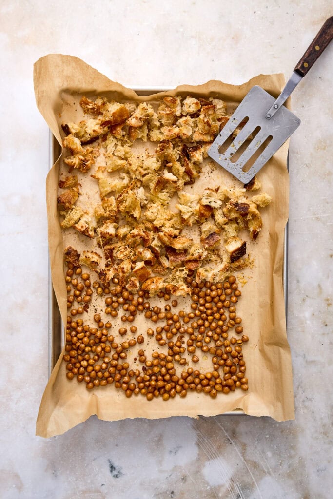 Freshly baked apple crisp with a caramel drizzle, served on parchment paper in a baking tray, with a spatula for serving.