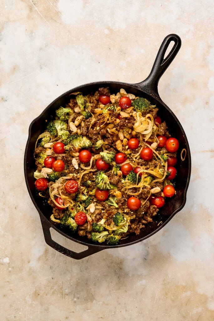 Delicious sausage and broccoli skillet with cherry tomatoes in a black skillet, showcasing fresh ingredients and vibrant colors.