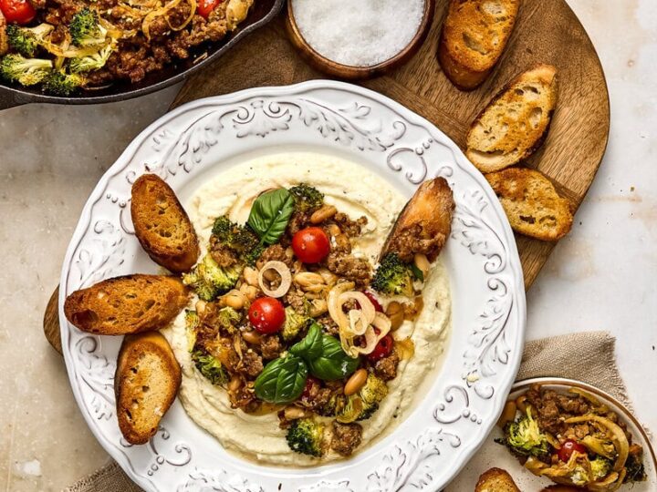 Colorful sausage and broccoli skillet served with toasted crostini, fresh basil, cherry tomatoes, and a side of salt in a rustic setting.