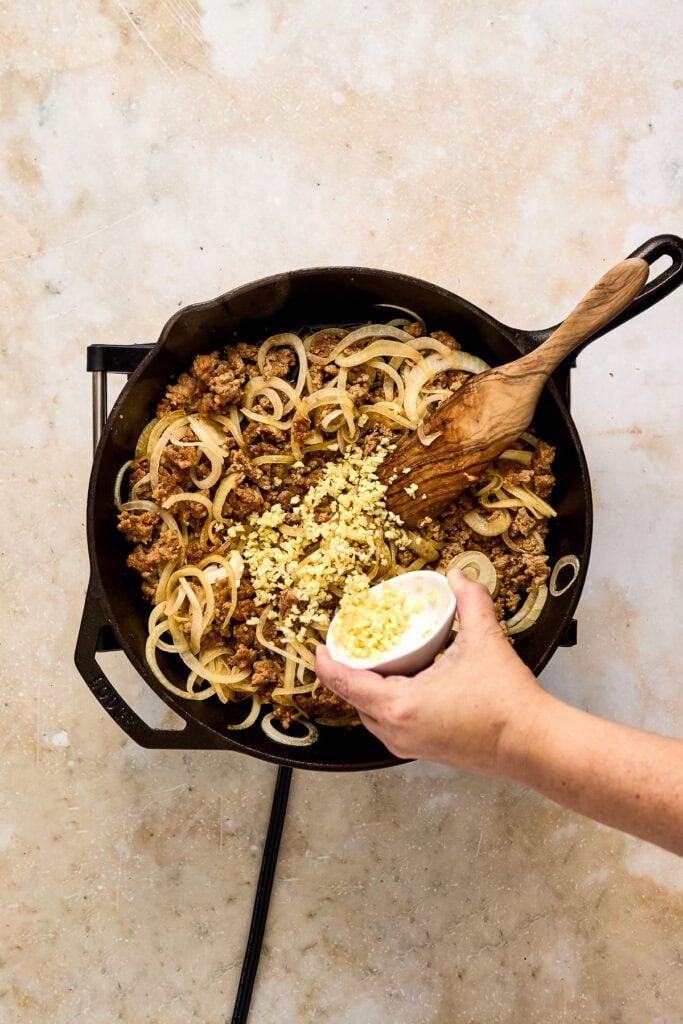 Cooking sausage and onions in a skillet with garlic and seasonings, ready to serve pasta dish.