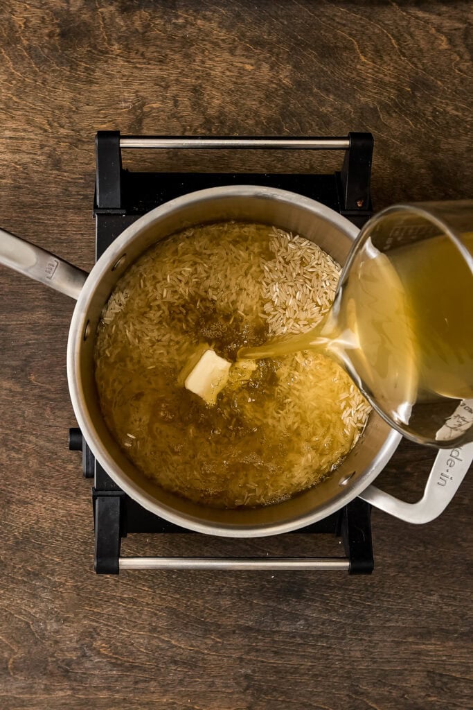 A pot of rice being cooked on a stove, with butter melting into the boiling rice, captured from above.