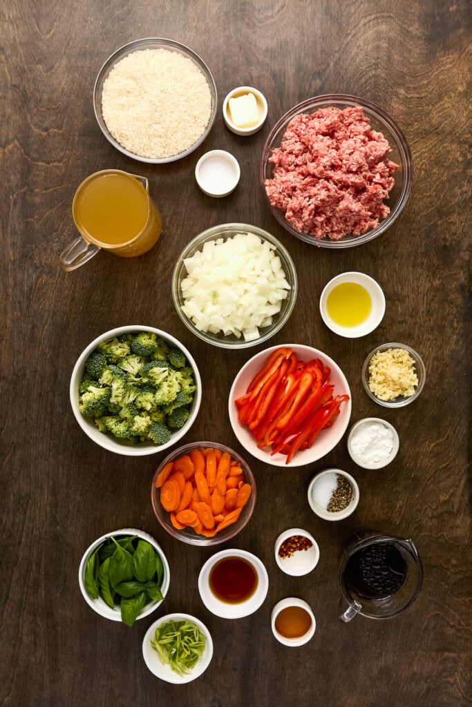 Assorted fresh ingredients for stuffed bell peppers including ground meat, rice, vegetables, and seasonings on a wooden surface.