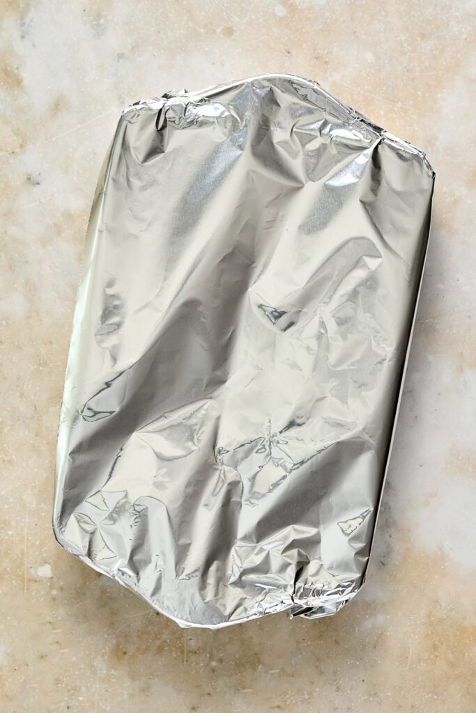 Baking dish covered with crinkled aluminum foil on a textured surface, ready for oven baking or storage.