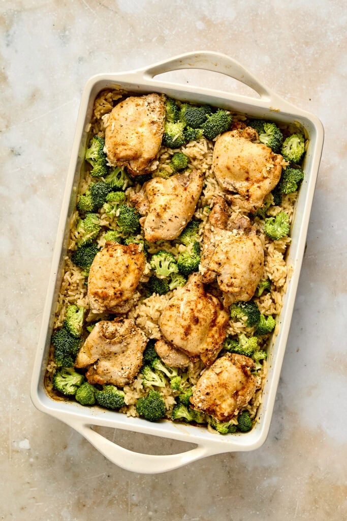 Baked chicken thighs with broccoli and rice in a white baking dish, served as a healthy meal option.