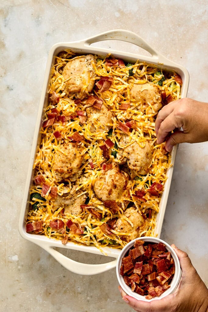 Delicious baked chicken and pasta casserole topped with crispy bacon bits and fresh herbs, served in a white baking dish.