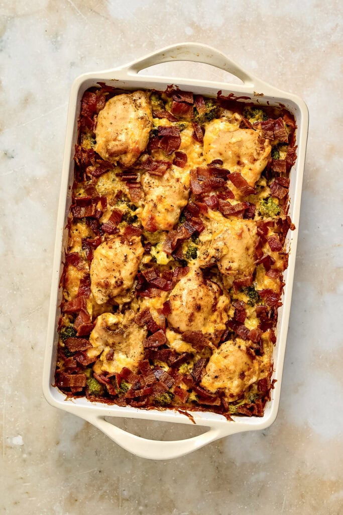 Baked chicken bacon ranch rice casserole with broccoli topped with crispy bacon bits in a white baking dish on a light surface.