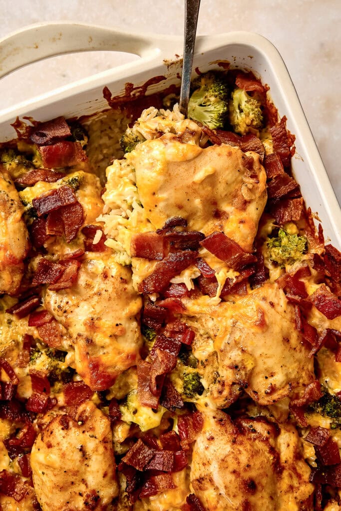 Delicious baked ranch chicken and broccoli casserole topped with melted cheese and crispy bacon bits, served in a white baking dish.
