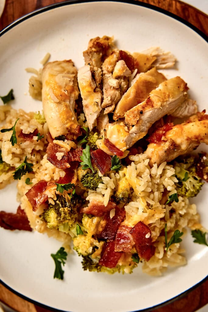 Delicious chicken and rice dish with broccoli, bacon, and fresh herbs served on a white plate.