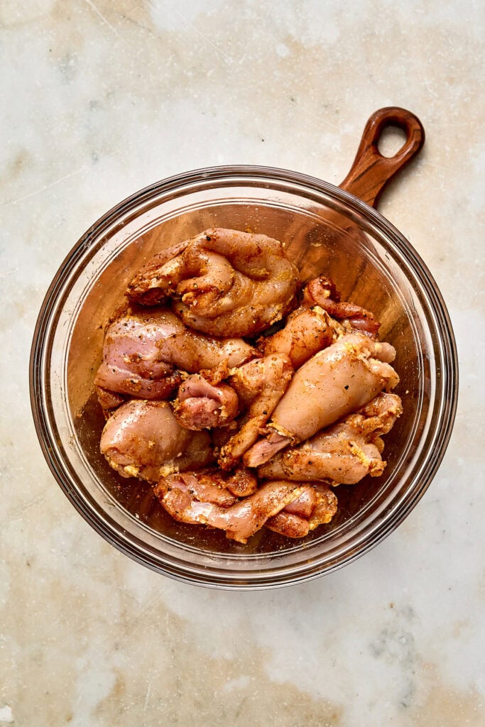 Raw chicken pieces in a glass bowl, ready for preparation or cooking, on a light textured surface.