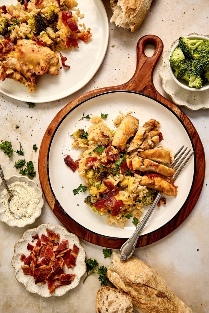 Delicious chicken bacon ranch rice casserole dish served with bacon, broccoli, and bread on a rustic table, perfect for a hearty meal.
