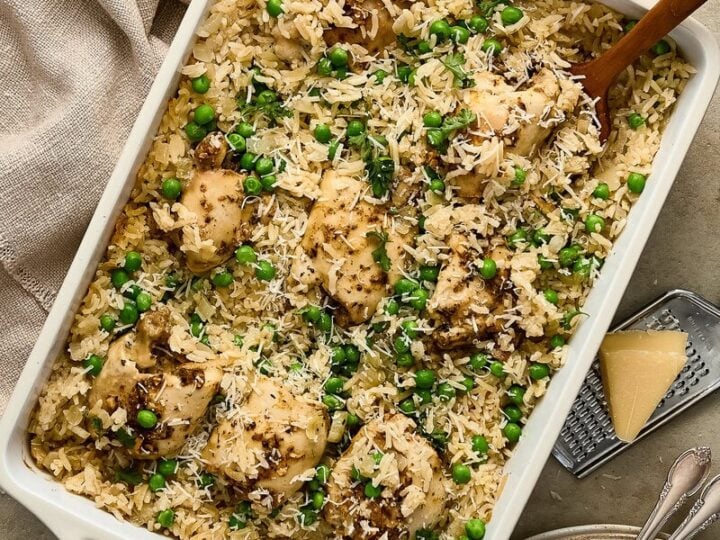 Delicious garlic chicken and rice casserole topped with green peas and herbs, served in a white baking dish with serving utensils.