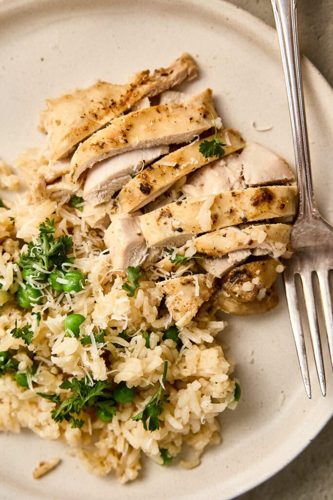 Herb-seasoned grilled chicken slices served with rice and fresh herbs on a white plate, close-up view.