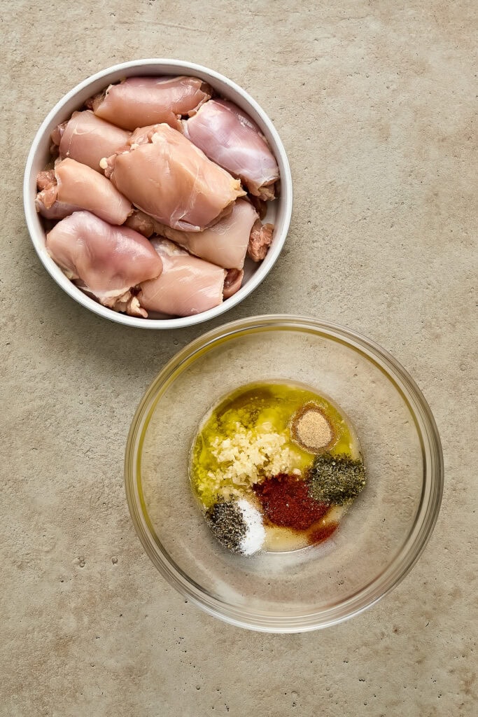 Raw chicken drumsticks in a bowl with spices and oil for preparing a flavorful dish.