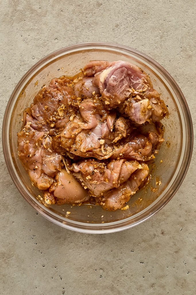 Raw chicken pieces marinated with spices and herbs in a glass bowl, ready for cooking or grilling.