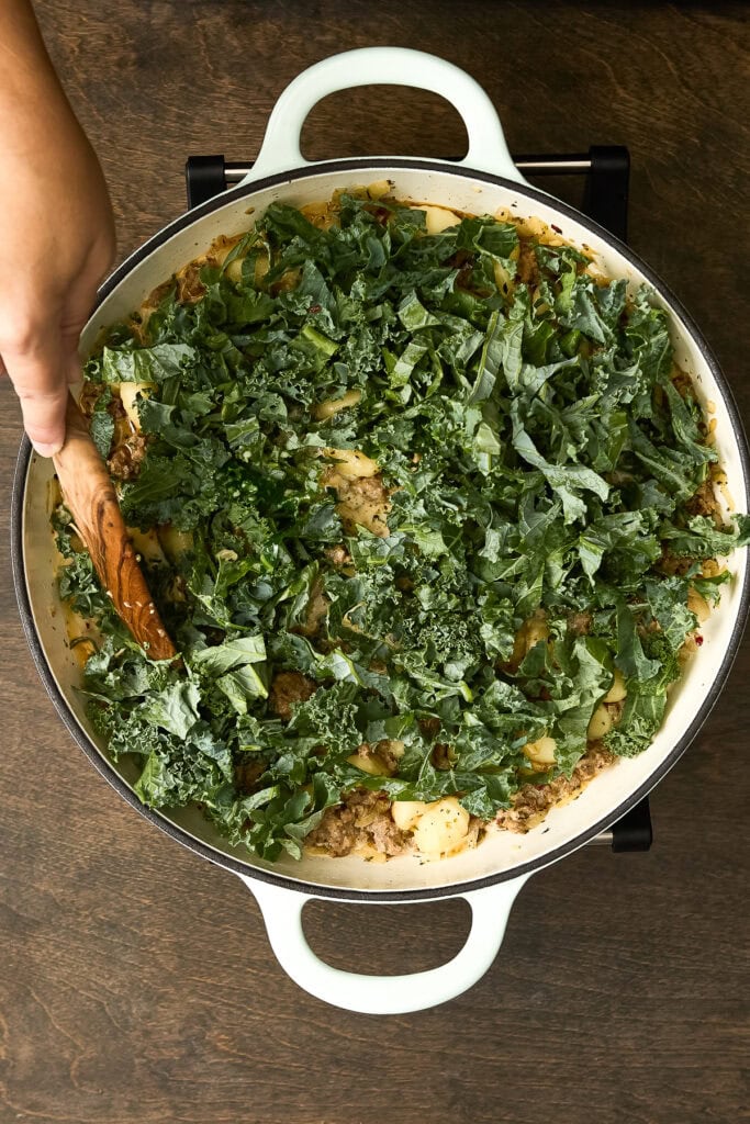 Close-up of a Zuppa Toscana Gnocchi dish topped with fresh kale in a white skillet, served on a dark wooden table.