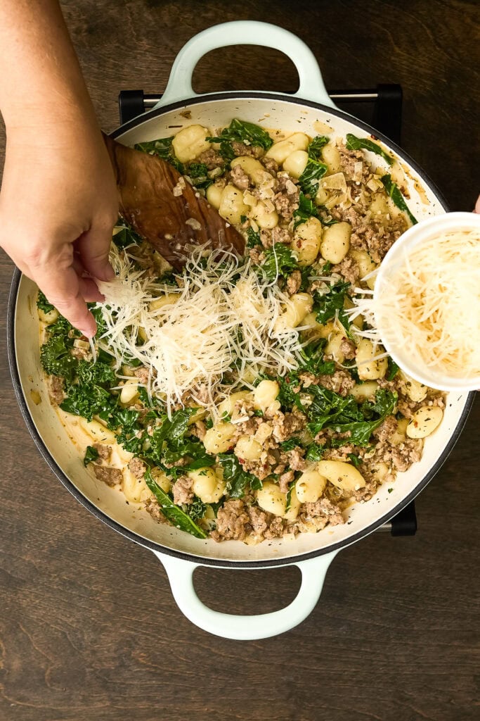 Close-up of Zuppa Toscana Gnocchi in a white skillet with ground sausage, kale, gnocchi, and shredded cheese, ready to serve.