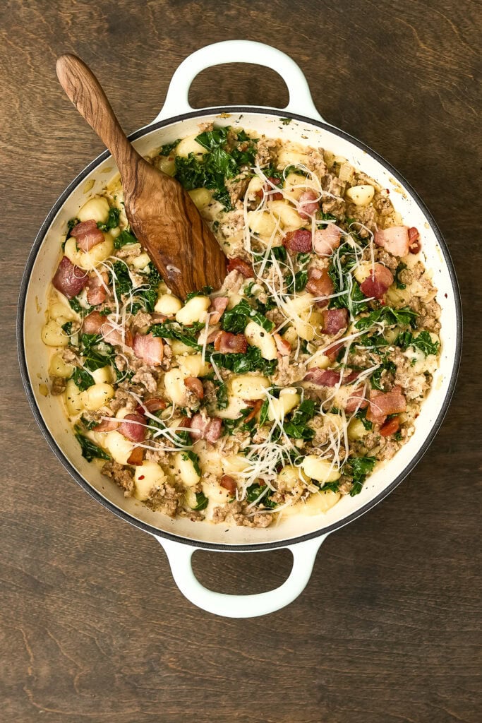 Delicious Zuppa Toscana Gnocchi with kale, sausage, and cheese in a white pot on a wooden surface, ready to serve.