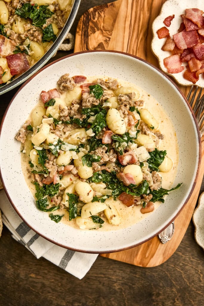 Creamy Zuppa Toscana gnocchi pasta with kale, sausage, and bacon served in a white bowl, perfect for comfort food lovers.