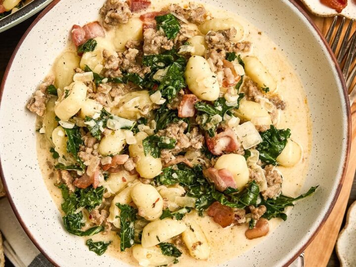Creamy Zuppa Toscana gnocchi pasta with kale, sausage, and bacon served in a white bowl, perfect for comfort food lovers.