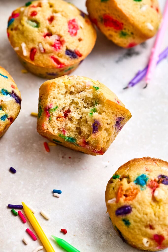 Close-up of freshly baked mini muffins with colorful sprinkles and one cupcake with a bite taken out, showcasing the moist interior.