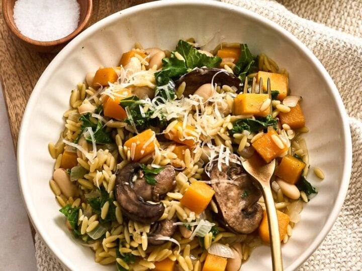 Delicious creamy butternut squash orzo with mushrooms, kale, and grated cheese served in a white bowl, perfect for a cozy meal.